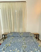 تخت خواب با روتختی طوسی رنگ و پرده سفید اتاق خواب خانه روستایی در سی سرا